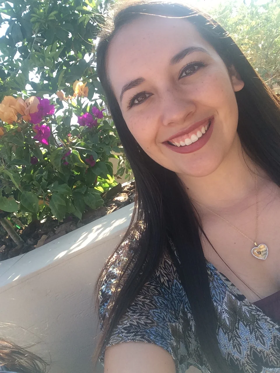 Olivia Ledezma smiling outdoors beside flowering bougainvillea